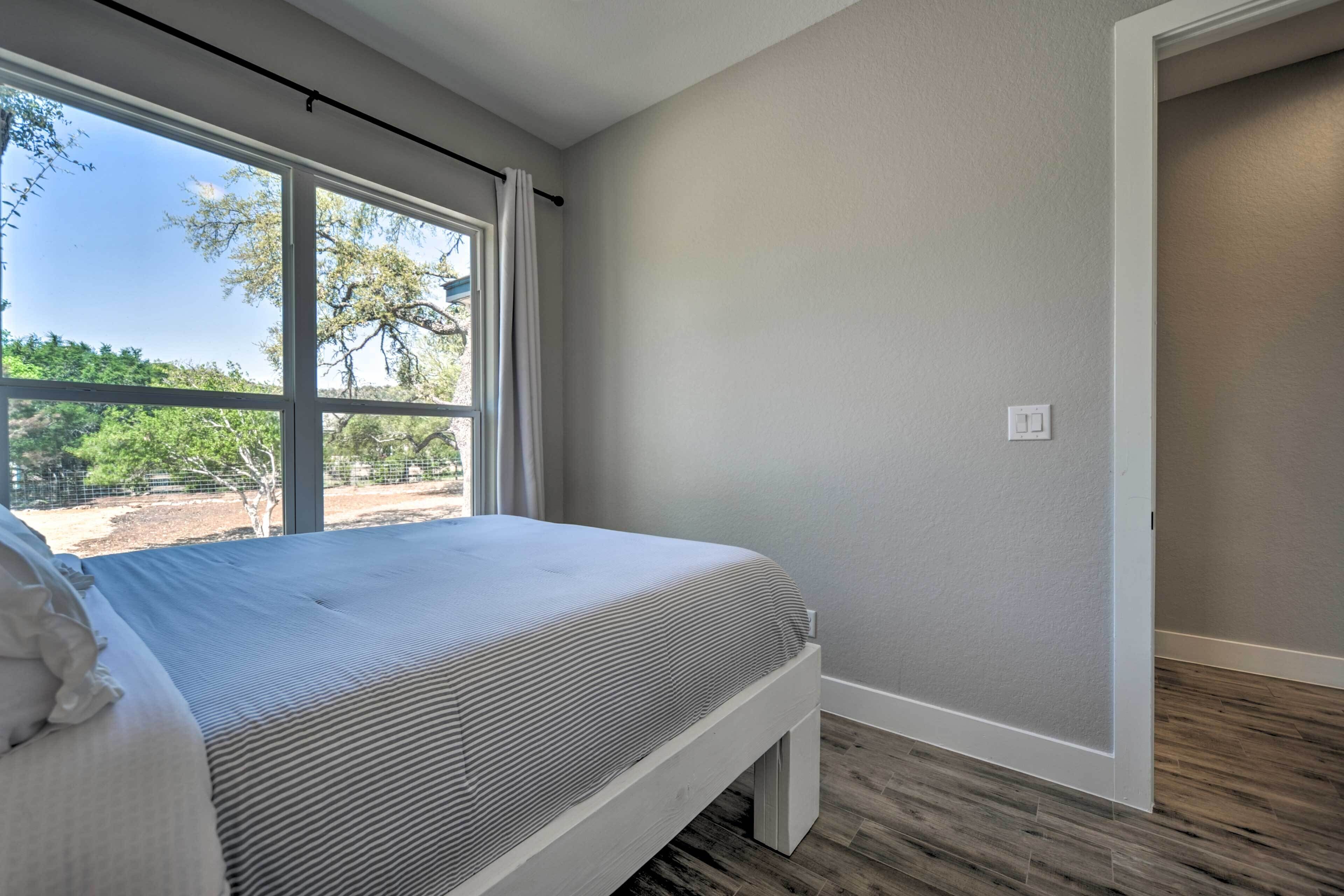 A bedroom with a large window, a bed with a white headboard, and a wooden floor.
