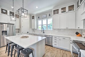 A modern kitchen with white cabinetry, a large island with bar stools, stainless steel appliances, and a herringbone tile backsplash. - Brand New Modern Canyon Lake Escape w/ Fire Pit! (Canyon Lake)