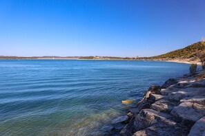 A coastal landscape with clear blue water, rocky shoreline, and distant hills. - Brand New Modern Canyon Lake Escape w/ Fire Pit! (Canyon Lake)