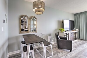 A dining area with a dark wooden table and white chairs, a wicker chandelier, and a large mirror on the wall.