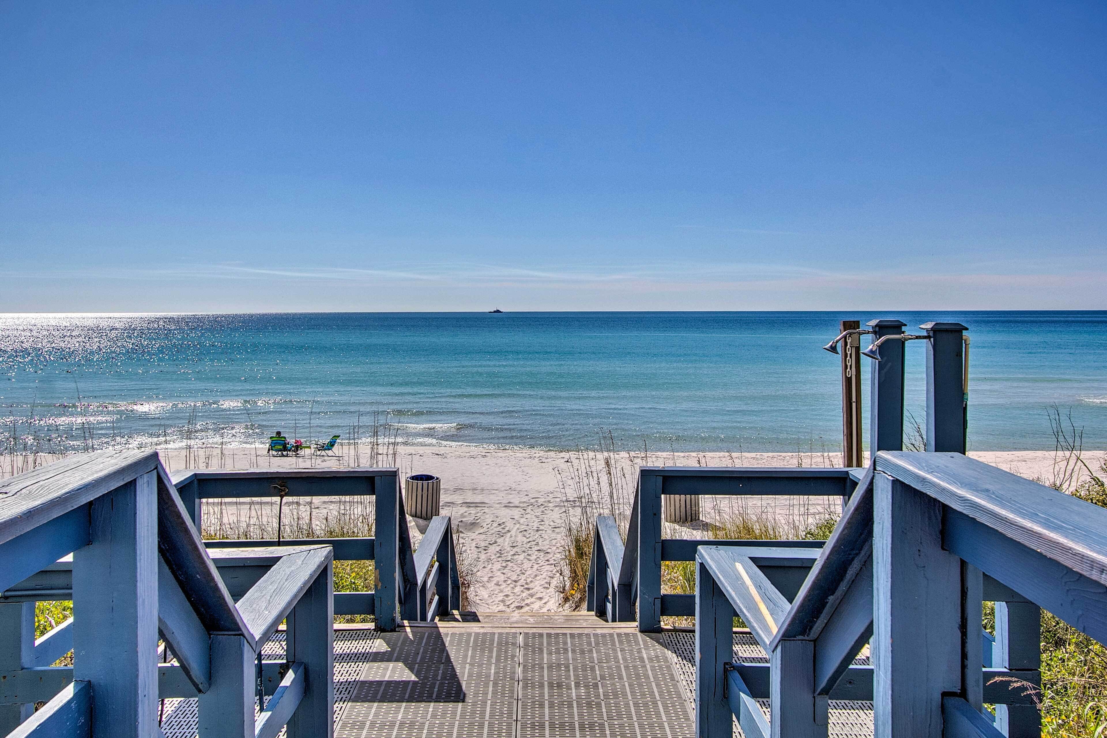 A wooden boardwalk leading to a sandy beach with a clear blue sky.