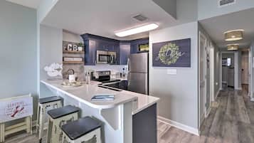 Uma cozinha moderna com ilha central, banquetas, micro-ondas e geladeira.