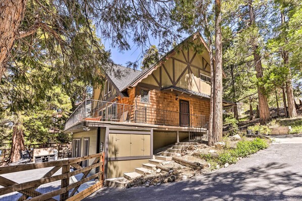 A two-story log cabin with a balcony, surrounded by tall pine trees.