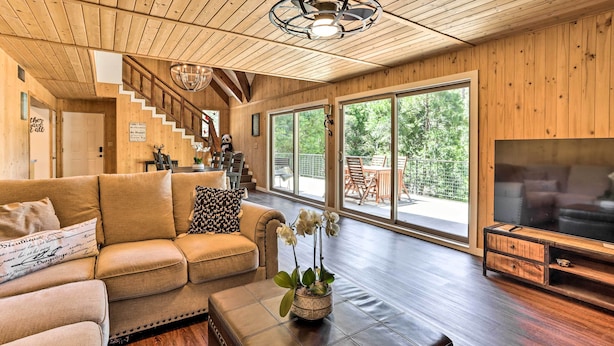 A spacious living room with a wooden ceiling, a large TV, and a staircase leading to an outdoor area. - Spacious Lake Arrowhead Cabin w/ Jacuzzi Spa! (Lake Arrowhead)