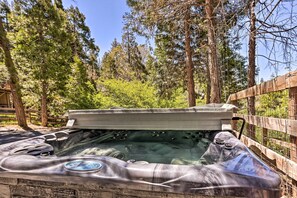 A hot tub in a wooded area with a wooden fence and trees in the background.