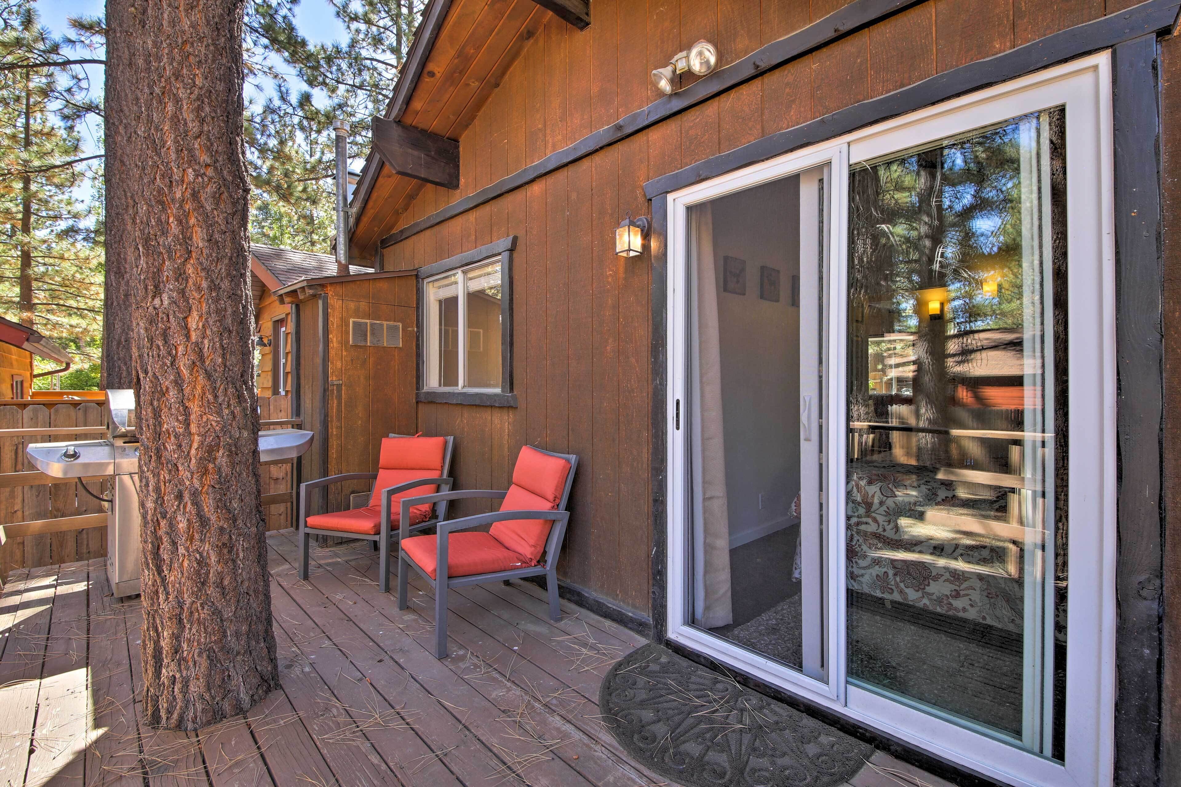 A wooden cabin with a deck, two chairs, and a large sliding glass door.