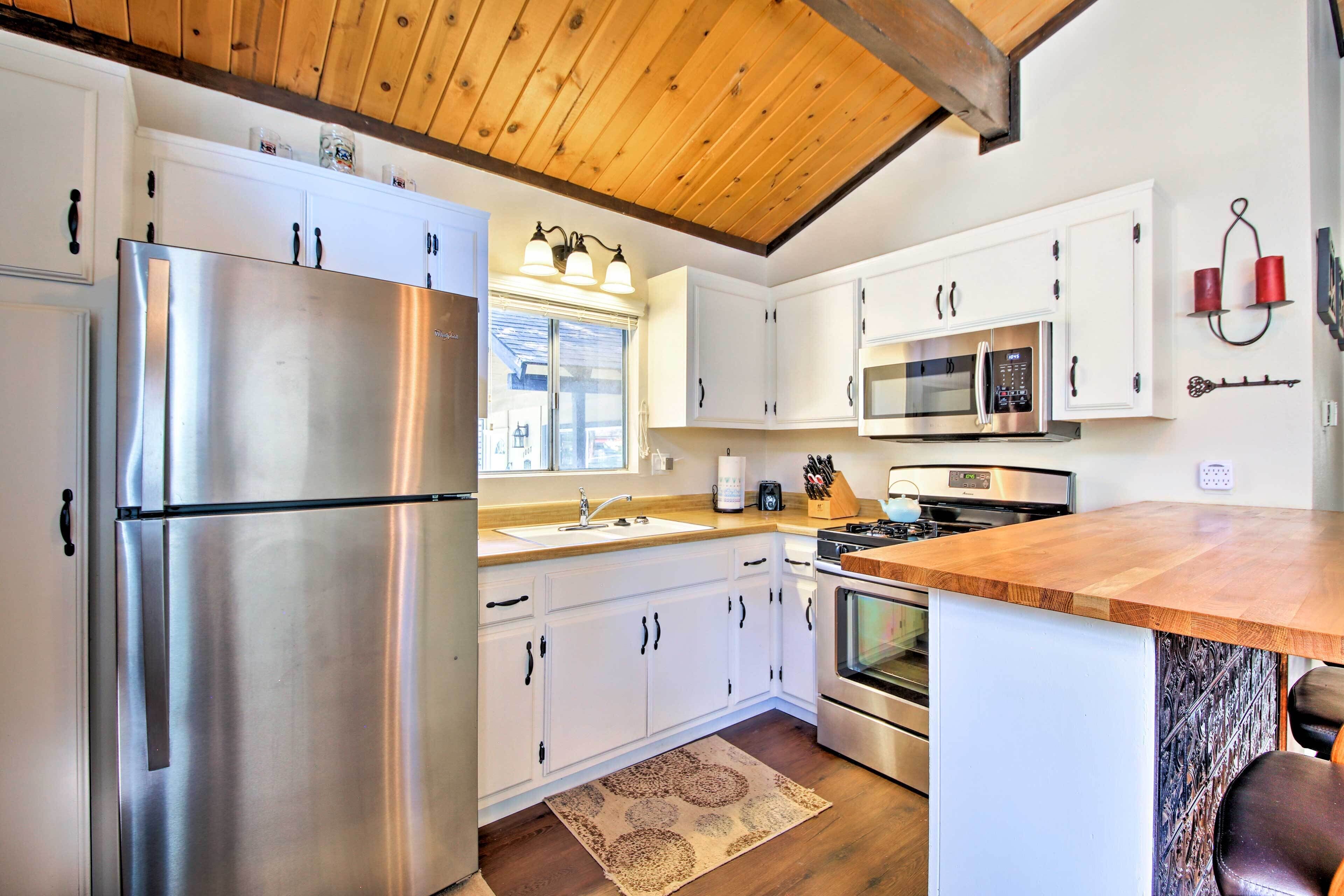 A modern kitchen with white cabinets, stainless steel appliances, and a wooden ceiling.