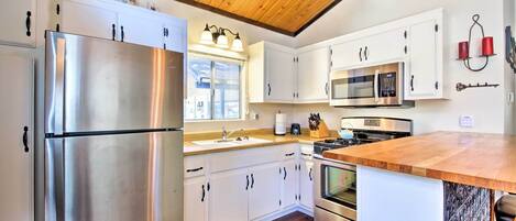 A modern kitchen with white cabinets, stainless steel appliances, and a wooden ceiling.
