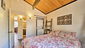 A bedroom with a bed, a wooden ceiling, a door leading to a bathroom, and a wall-mounted shelf.