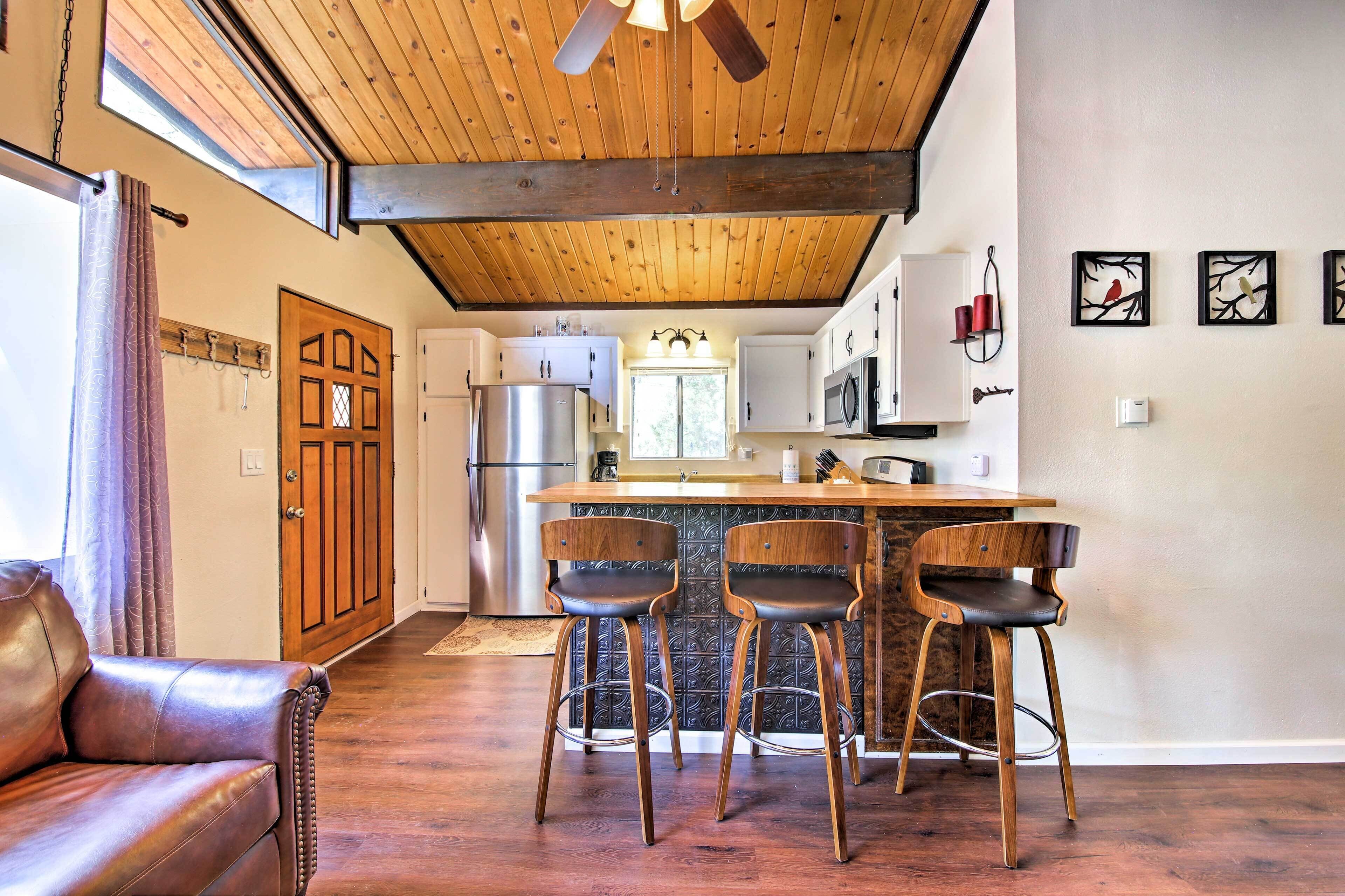 A kitchen with a wooden ceiling, a bar area with stools, a refrigerator, and a microwave.