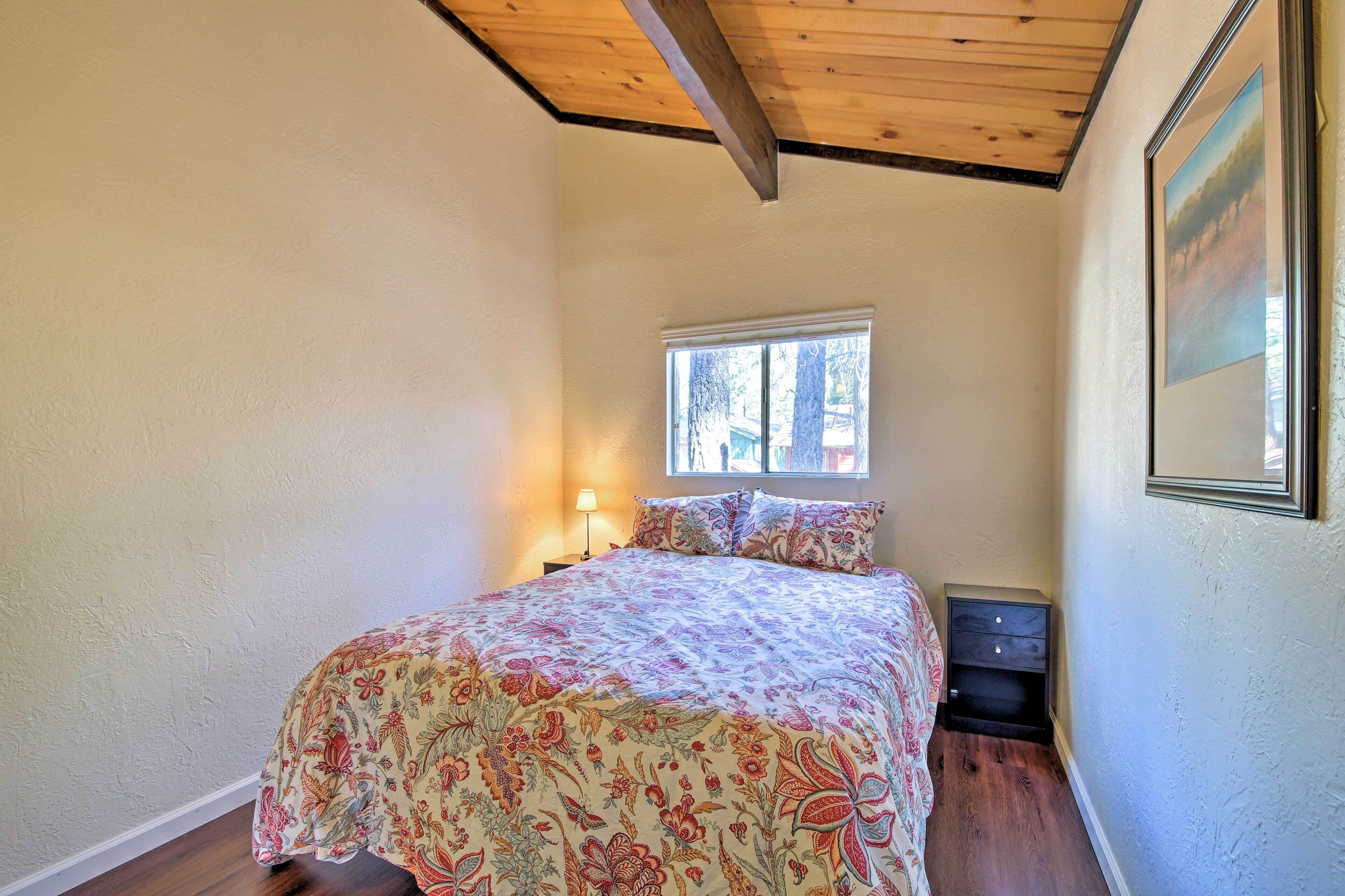 A bedroom with a bed, a nightstand, a window, and a framed picture on the wall.