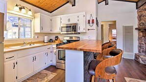 A modern kitchen with white cabinets, stainless steel appliances, a wooden island with bar stools, and a stone accent wall.