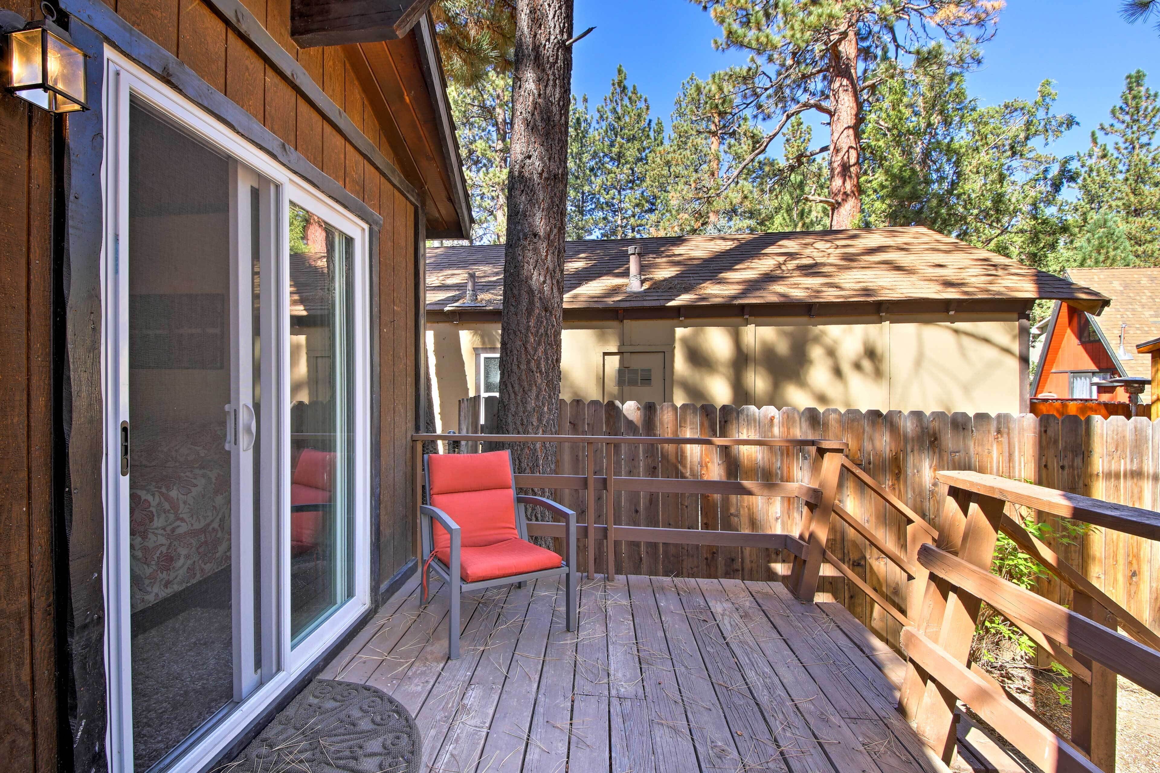 A wooden deck with a red chair, a wooden fence, and a building with a sloped roof.