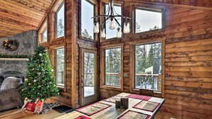 A cozy cabin interior with a wooden interior, a Christmas tree, a fireplace, and large windows offering views of the forest. - Luxury Mountain Getaway in Fairplay w/ Deck! (Fairplay)