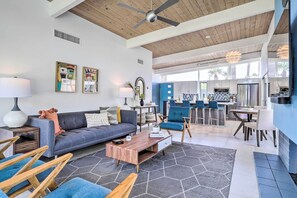 A modern living room with a gray sofa, wooden coffee table, and blue chairs. A kitchen is visible in the background with blue cabinets and a stainless steel refrigerator. - Pool & Mountain Views: Palm Springs Home! (Palm Springs)