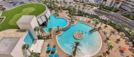 A hotel with a large swimming pool, multiple lounge areas, and a landscaped garden.