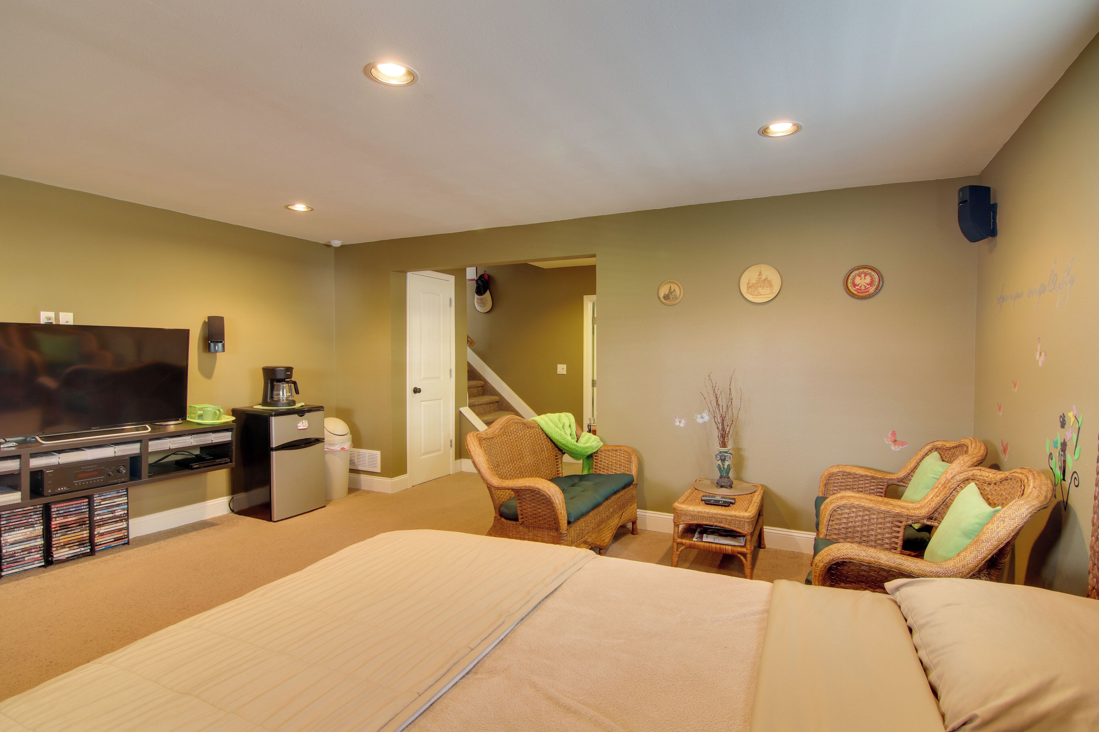 A hotel room with a bed, two wicker chairs, a small table, a television, a refrigerator, and a coffee maker.