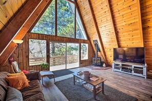 A spacious loft with a high ceiling, large windows, a cozy seating area, and a fireplace. - Running Springs Cabin w/ Large Deck + View! (Running Springs)