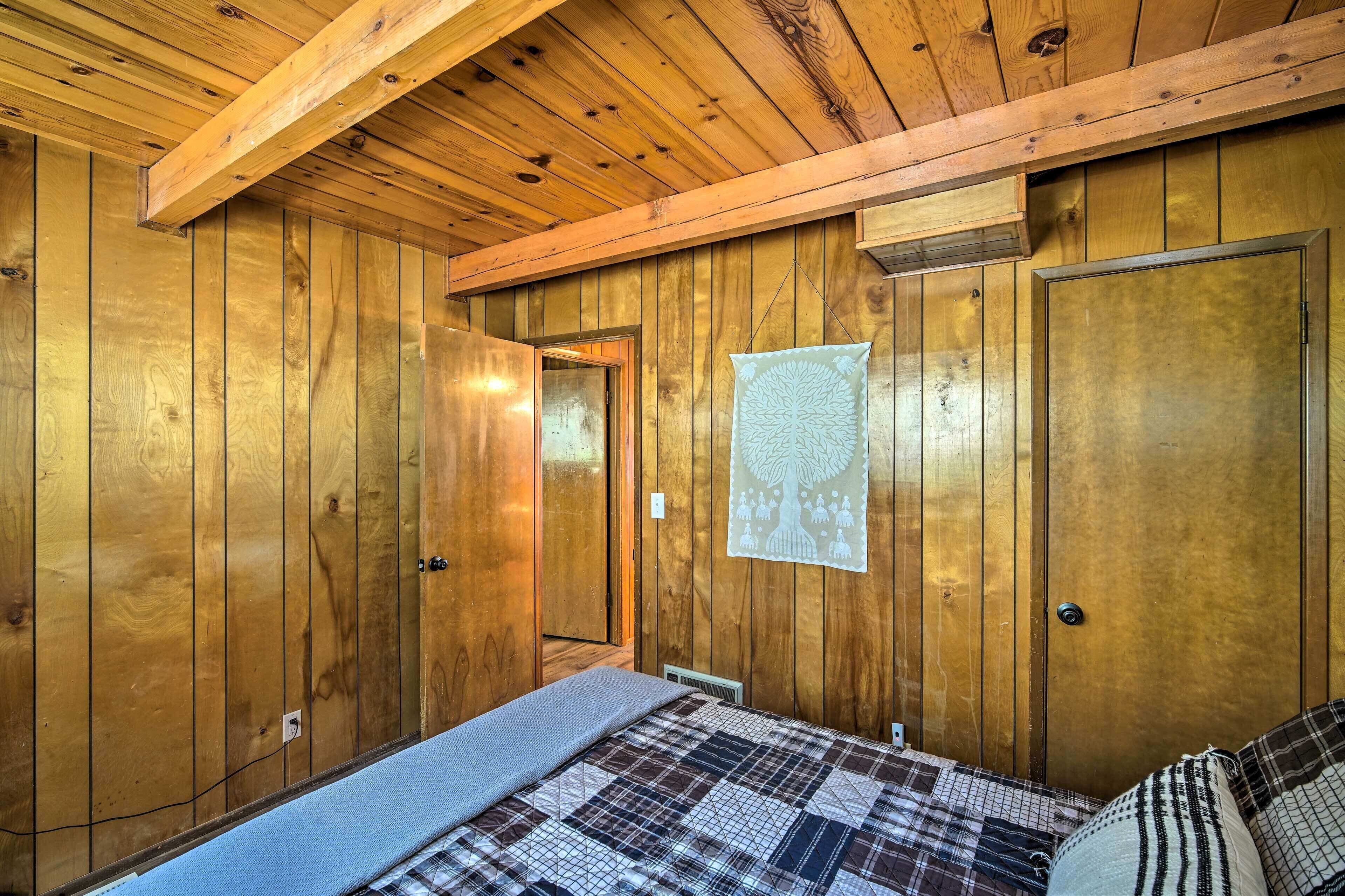 A wooden-paneled bedroom with a bed, a door, and a wall-mounted light fixture.