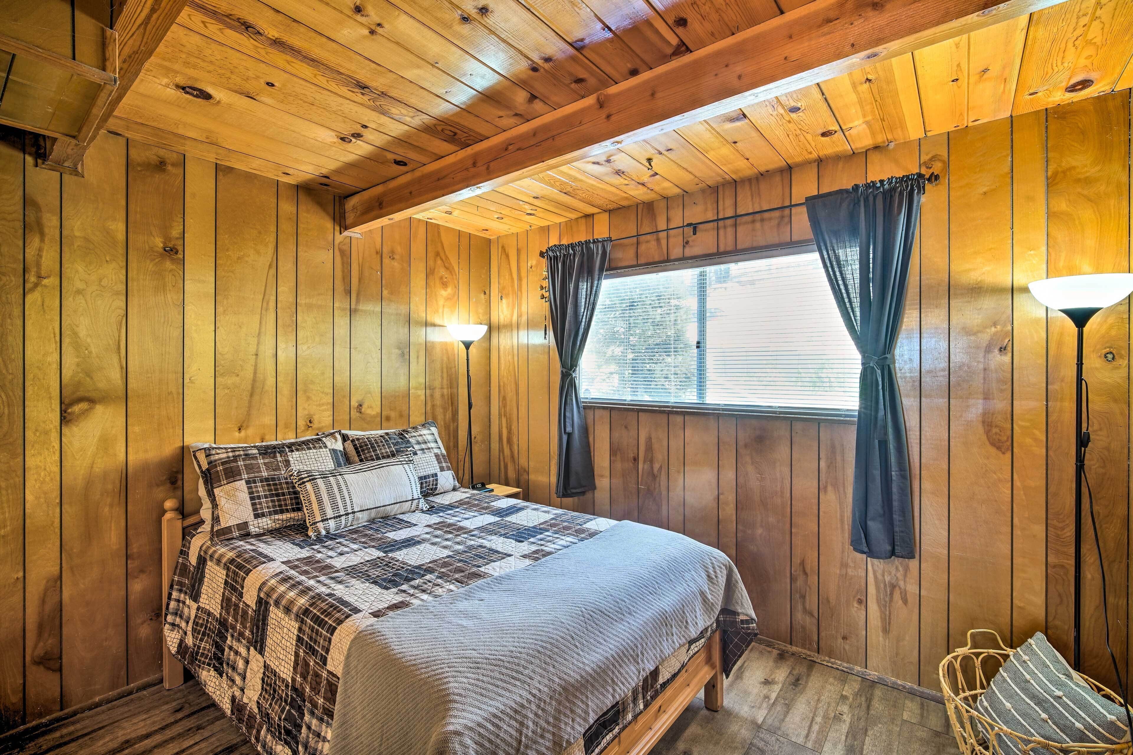 Een slaapkamer met houten lambrisering, een bed, een raam met gordijnen, een lamp en een stoel.