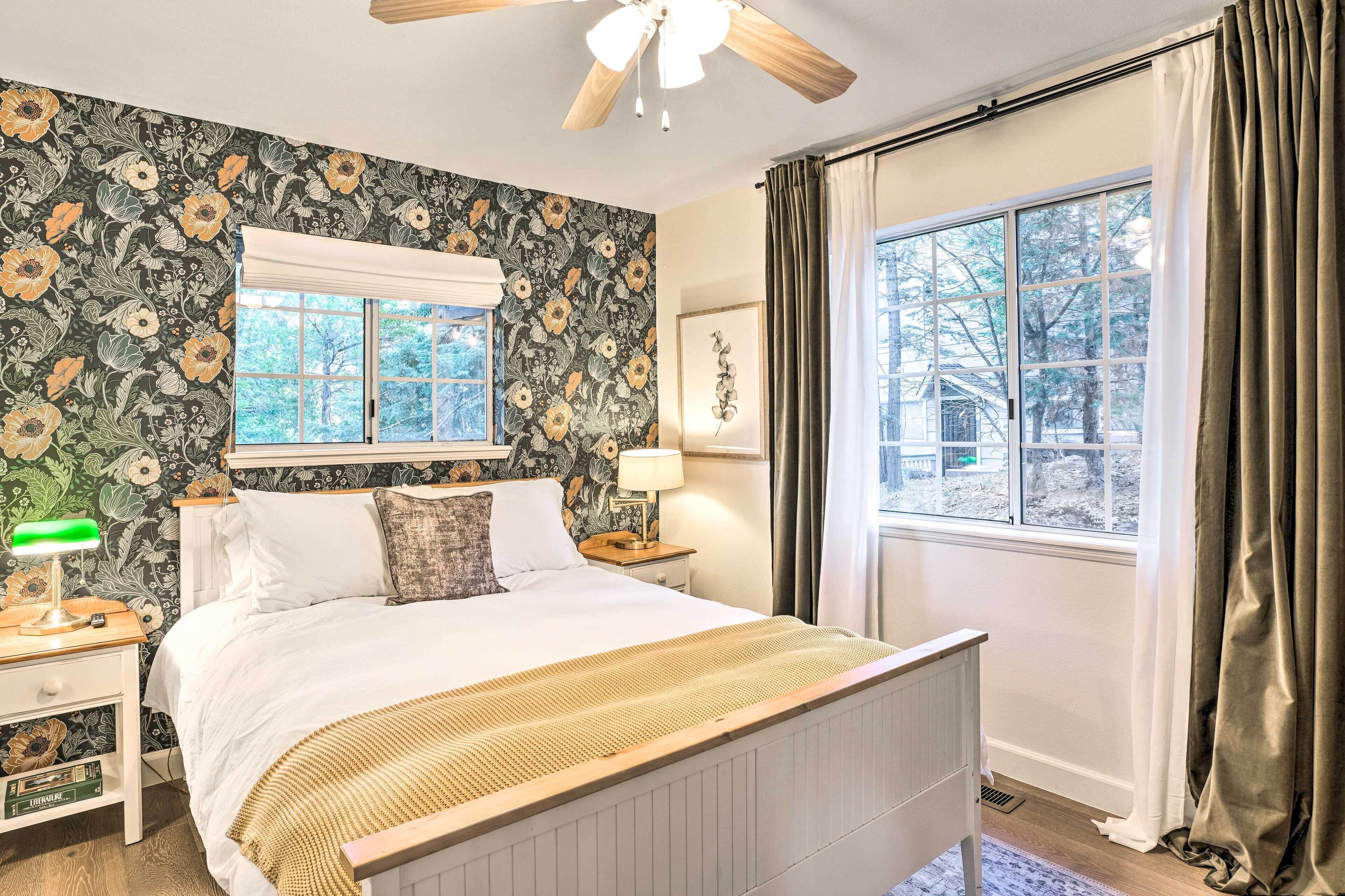 A bedroom with a bed, a nightstand, a lamp, a window with curtains, and a ceiling fan.