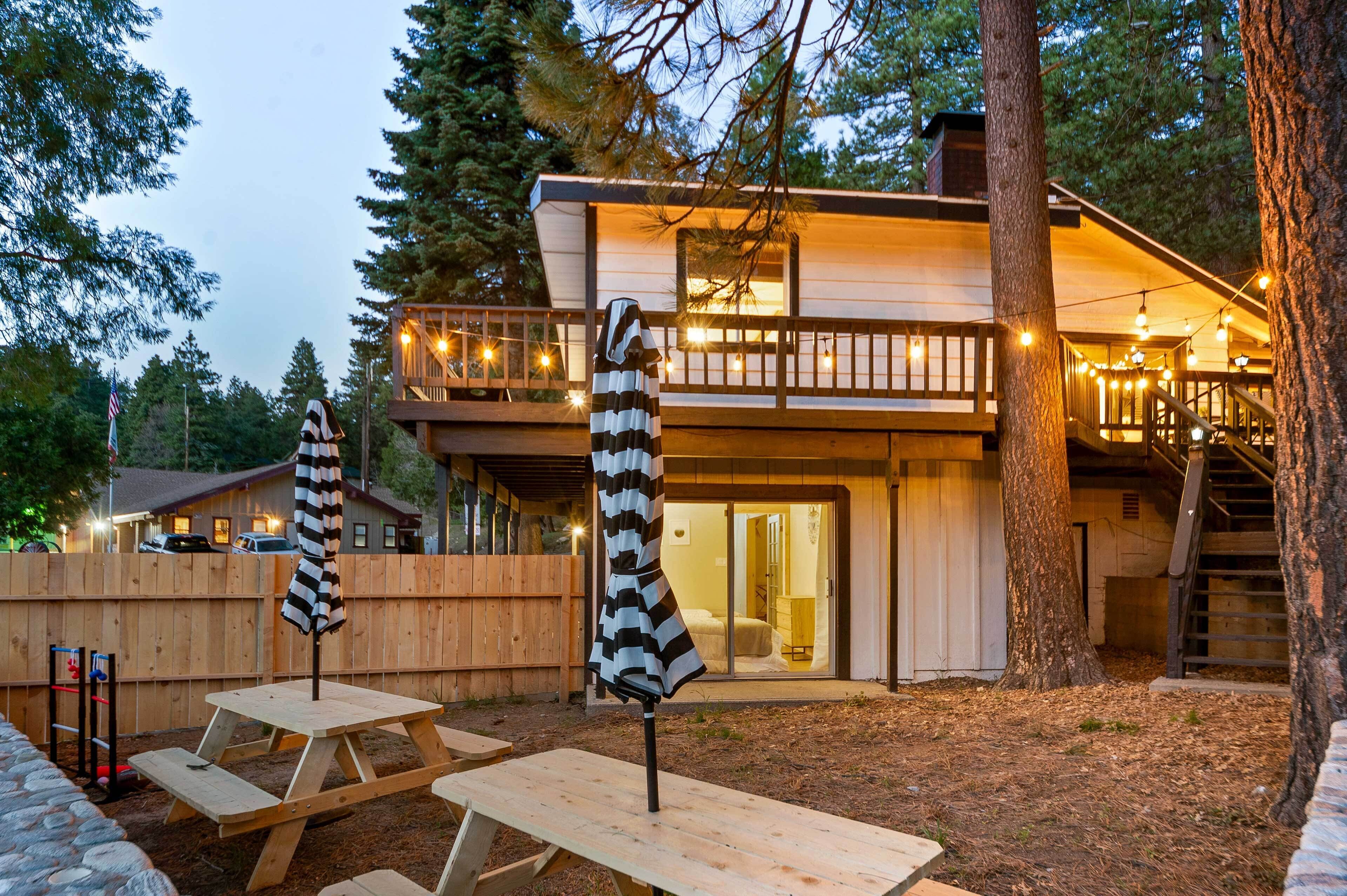 A two-story wooden cabin with a balcony, picnic tables, and string lights.