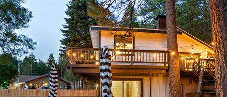 A two-story wooden cabin with a balcony, picnic tables, and string lights.