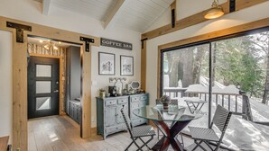 Un intérieur chaleureux avec une table à manger en verre, des meubles en bois et un panneau indiquant l’emplacement du bar à café.