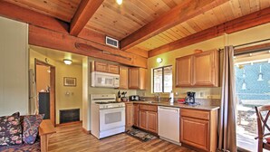 A kitchen with wooden cabinets, a stove, microwave, and dishwasher. There is a wooden ceiling and a window with curtains.