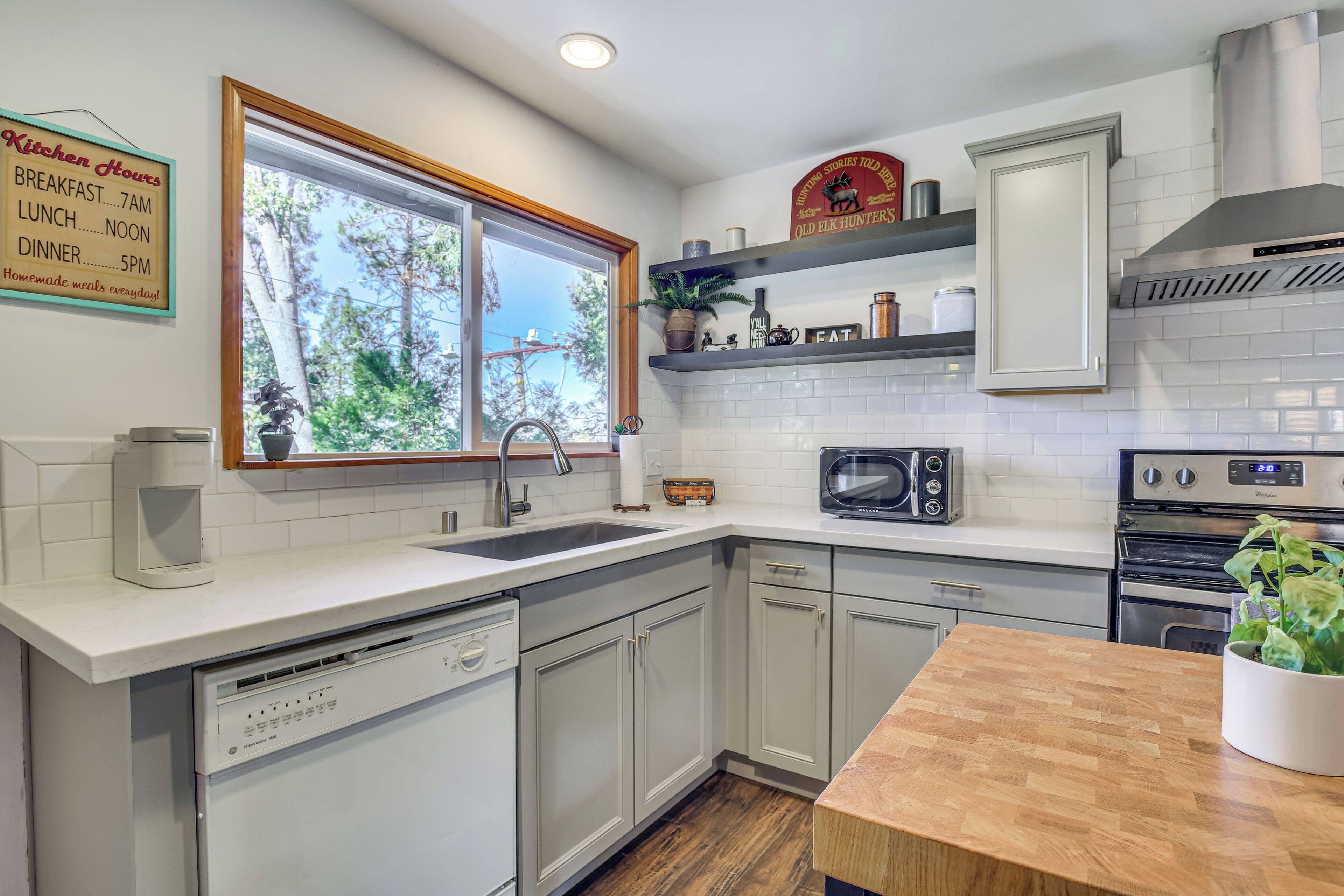 Una cocina moderna con armarios blancos, encimera de madera, microondas integrado y lavavajillas.