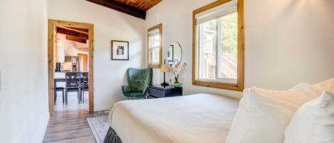 Une chambre avec un grand lit, des poutres apparentes en bois au plafond, un bureau avec une chaise et une fenêtre donnant sur l’extérieur.