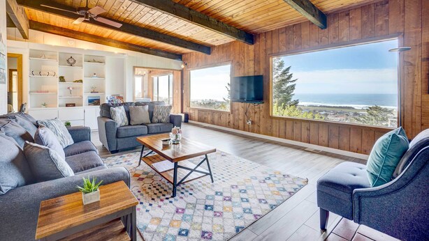 Un salon spacieux doté d’une grande fenêtre, de poutres apparentes en bois et d’un coin salon confortable.