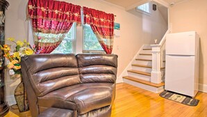 A living room with a brown leather sofa, a white refrigerator, and a staircase leading to an upper level. - Charming Yonkers Retreat - 10 Mi to Central Park! (Yonkers)