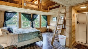 A log cabin bedroom with a bed, a ladder, a bathroom, and a view of the outdoors. - 3 Cabins! Lakefront Reunion Retreat in Rocky Mount (Rocky Mount)