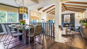 A spacious dining area with a high ceiling and exposed beams, a fireplace, and a view of the outdoors. - Lake Arrowhead Retreat w/ Decks + Mountain Views! (Lake Arrowhead)