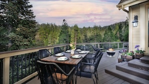An outdoor deck with a dining table set for four, surrounded by chairs, with a fire feature and potted plants. - Lake Arrowhead Retreat w/ Decks + Mountain Views! (Lake Arrowhead)