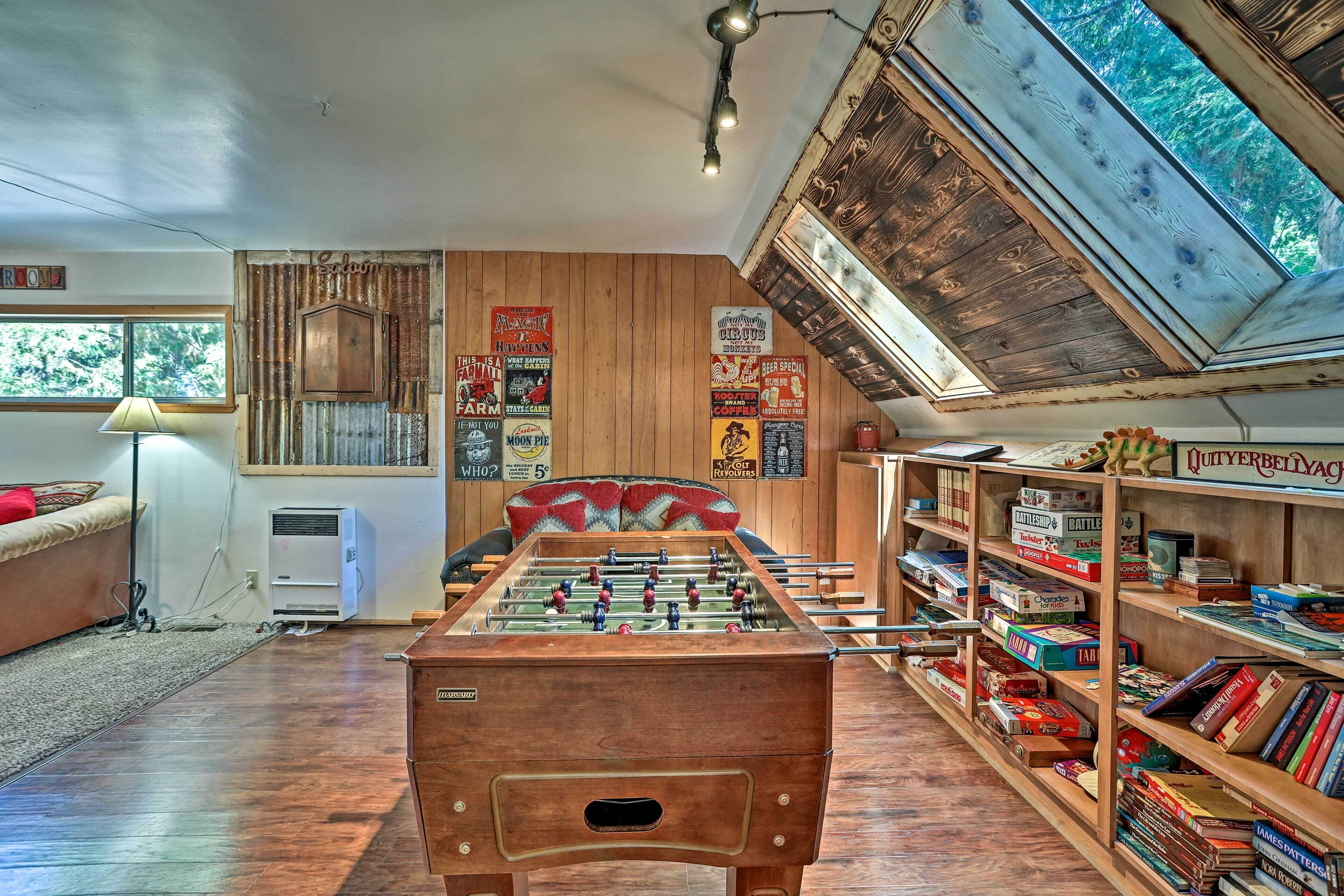 A cozy room with a foosball table, wooden shelves with board games, and a window with a view of trees.