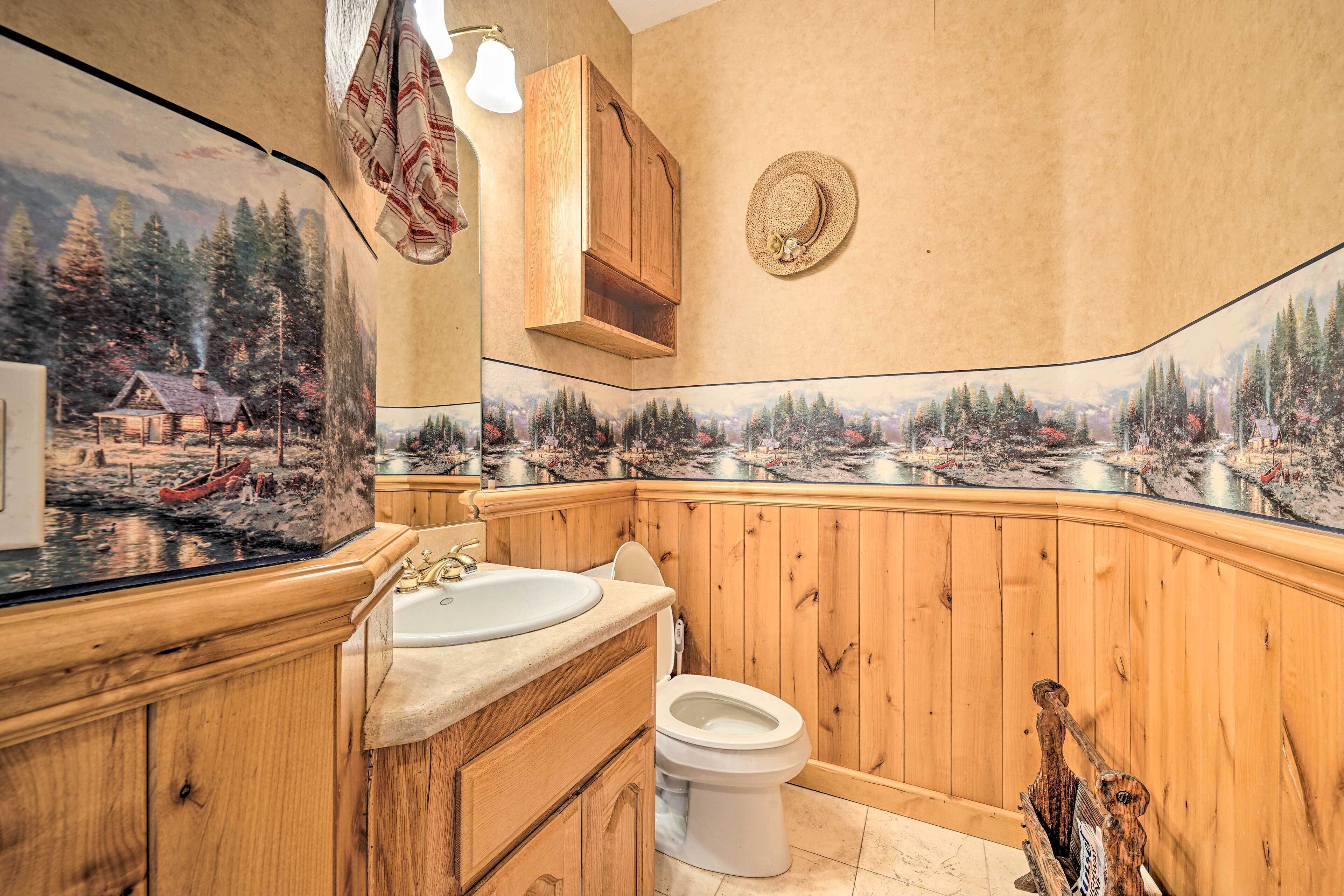 A bathroom with wooden paneling, a sink, toilet, and a large mirror with a scenic view.
