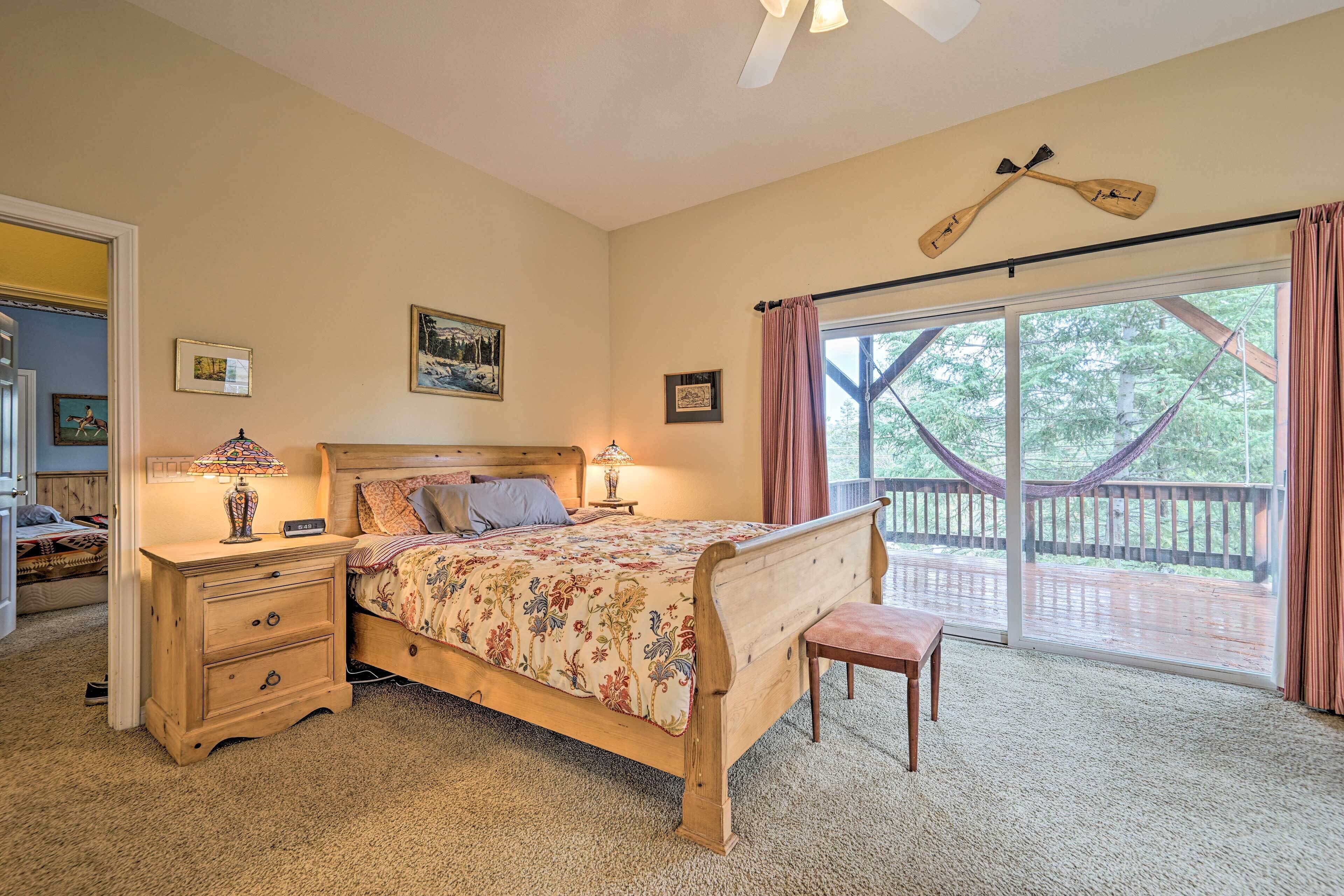 A bedroom with a wooden bed, a nightstand, a bench, and a large window with a view of a deck.