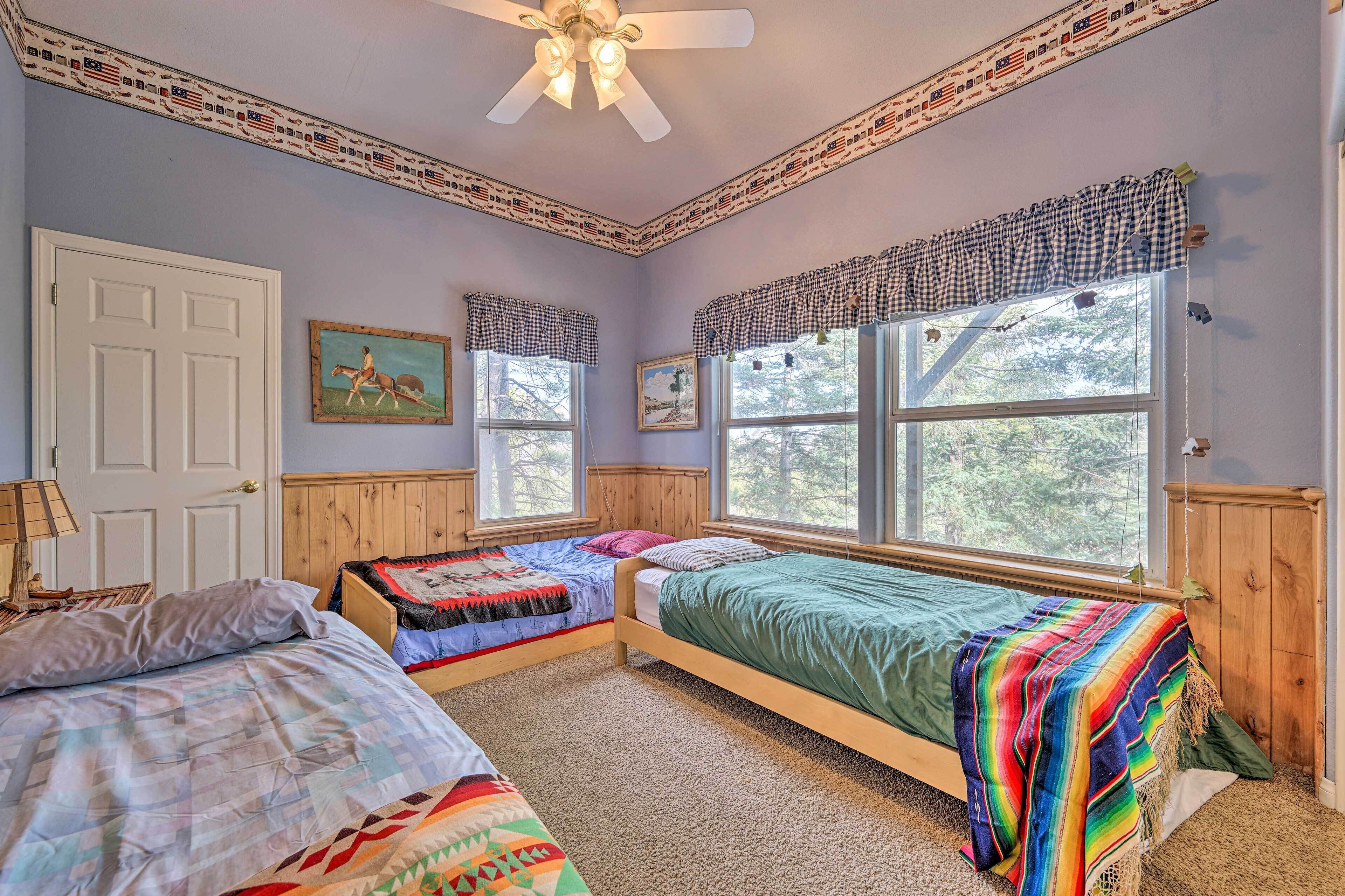 Ein Schlafzimmer mit zwei Betten, großen Fenstern, einem Deckenventilator und einer Tür.