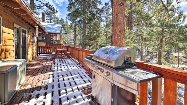 A wooden deck with a grill and a covered seating area, surrounded by tall pine trees. - Walk to Lake: Rustic Home w/ Deck in Fawnskin (Fawnskin)