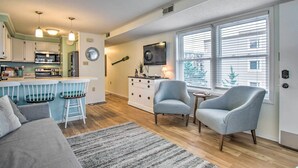 A compact living space with a kitchenette, a dining area with bar stools, a sofa, two armchairs, and a large window with blinds. - Walk to Maryland Beach: Coastal Condo w/ Balcony (Ocean City)