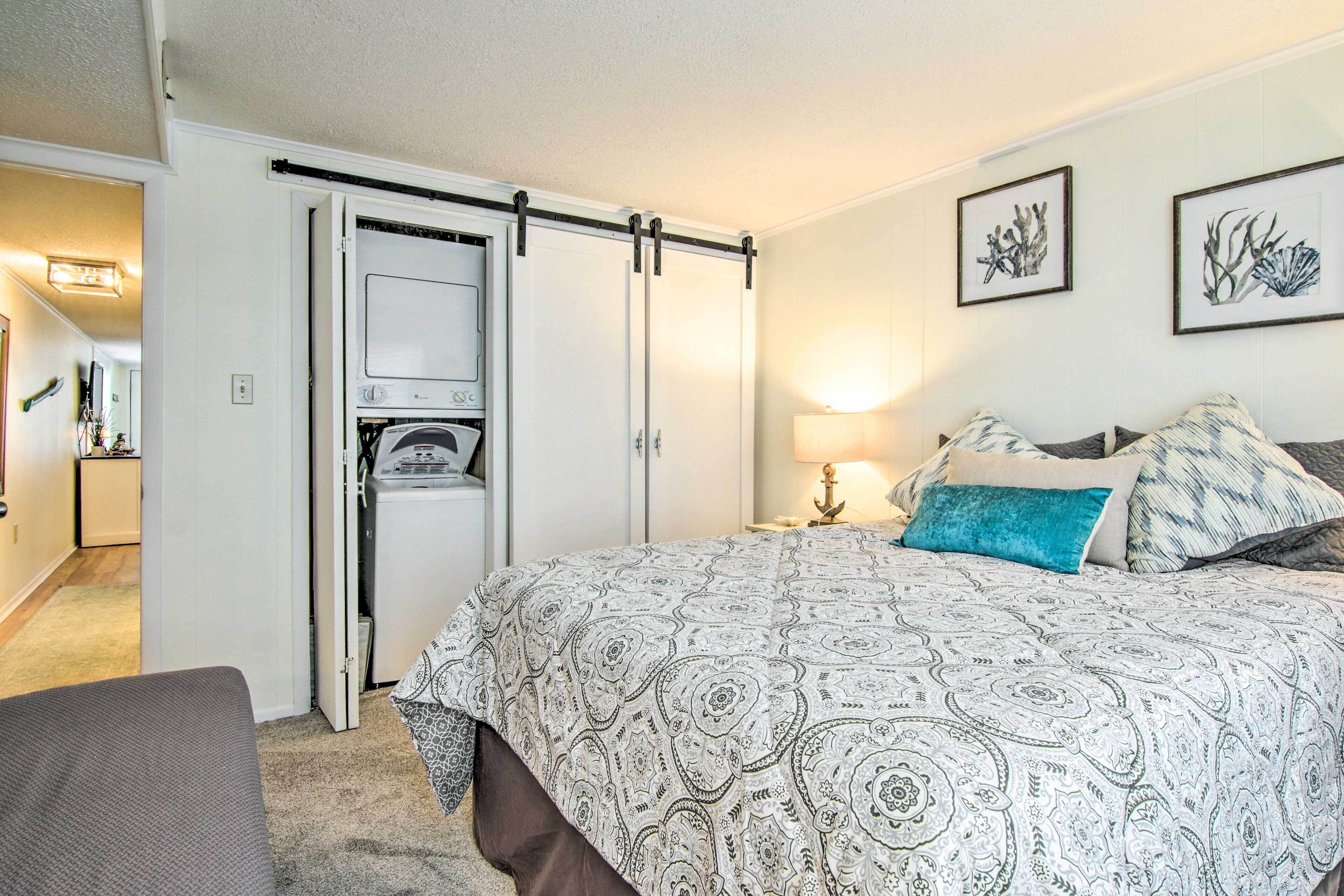 Un dormitorio con cama, armario, lavadora y mesita de noche con lámpara.