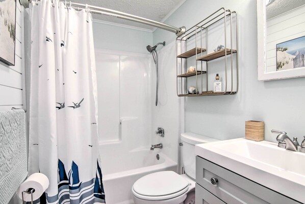 Ein Badezimmer mit Duschvorhang, Toilette, Waschbecken und Regalen.