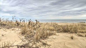 A beach with sand and sparse vegetation under a cloudy sky. - Walk to Maryland Beach: Coastal Condo w/ Balcony (Ocean City)