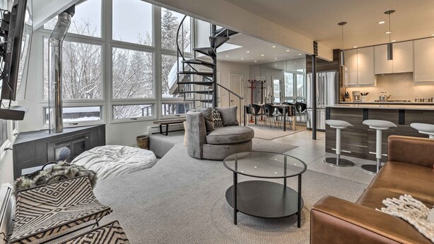 A modern interior with a spiral staircase, large windows, a cozy seating area, and a kitchen with bar stools. - Vail Condo w/ Mtn-view Deck - Steps to Ski Shuttle (Vail)
