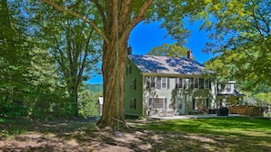 Ein zweistöckiges Haus mit einem großen Baum davor, umgeben von üppiger Vegetation.