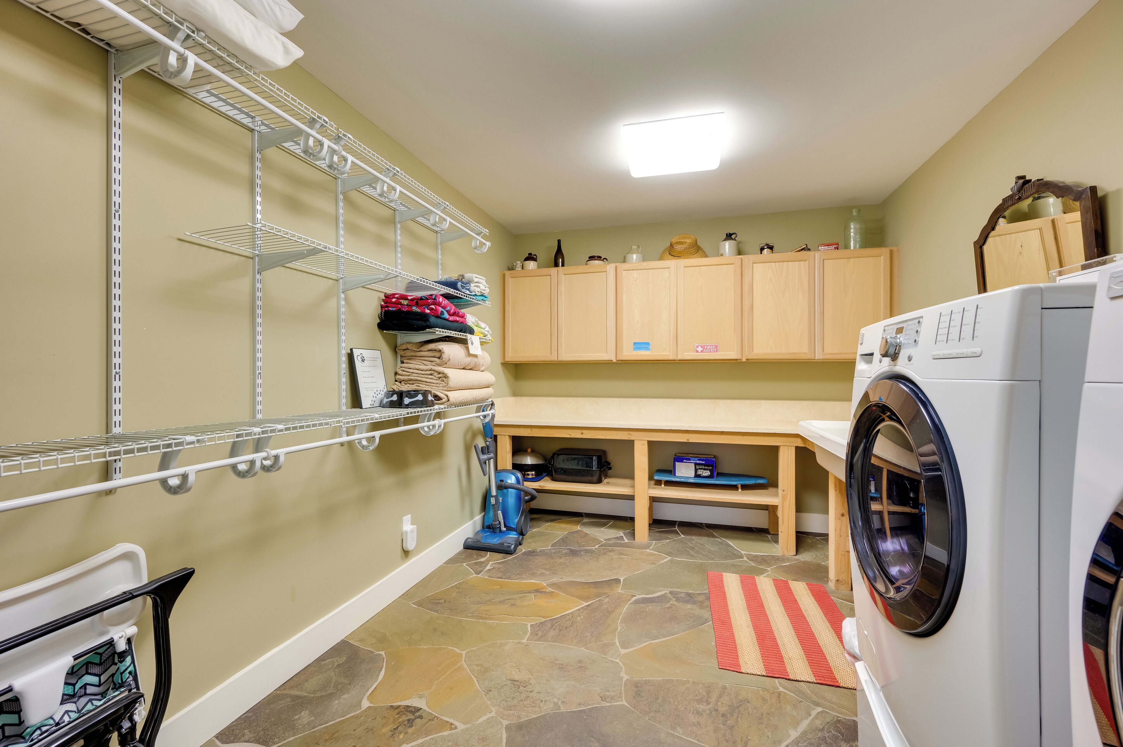 Une buanderie équipée d’un lave-linge, d’étagères, d’un aspirateur et d’armoires en bois.