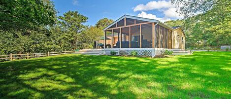 A wooden cabin with a large porch, surrounded by a well-maintained lawn and trees.