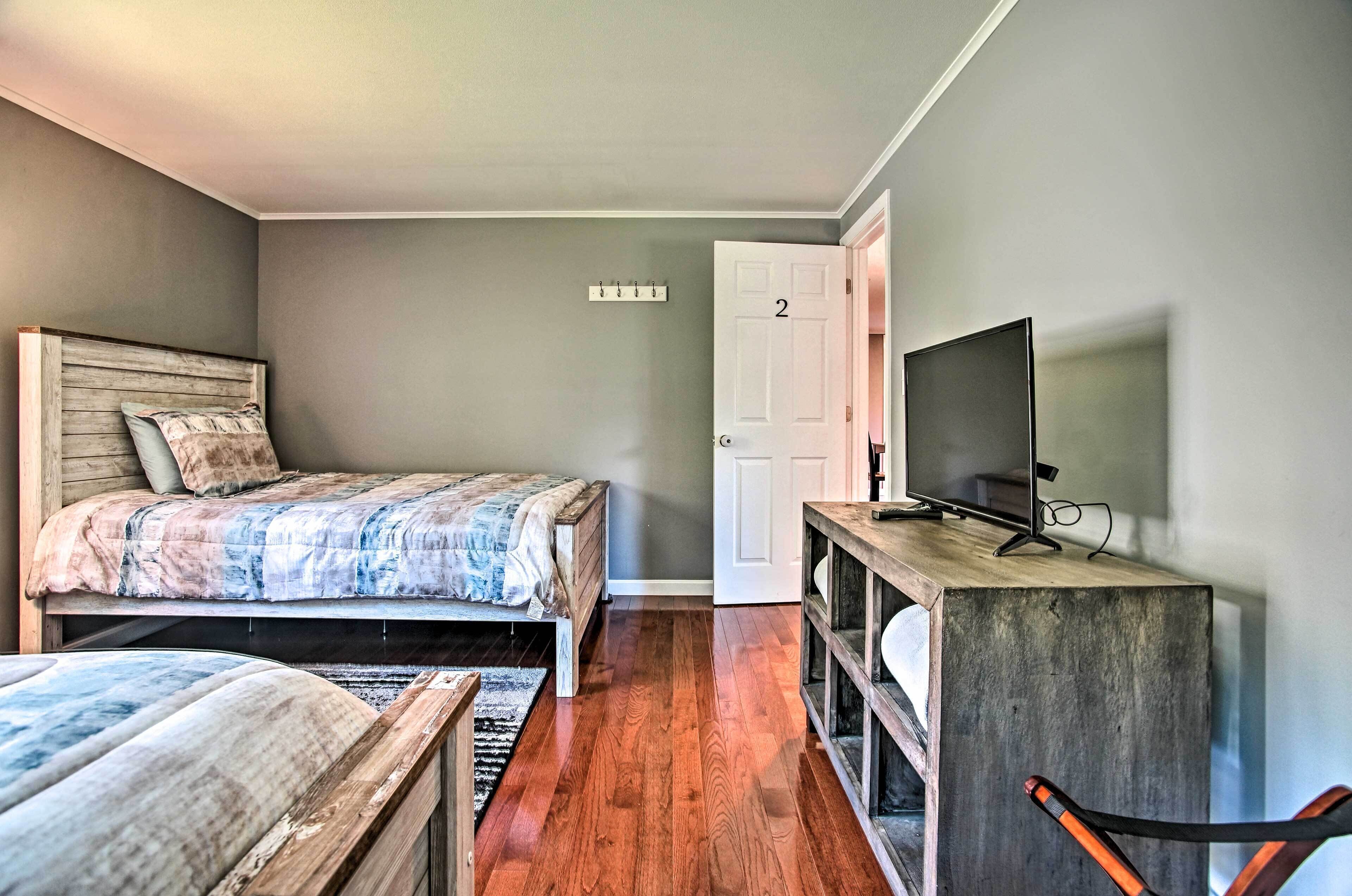 A bedroom with a bed, a TV on a wooden stand, a door with a number, and a coat rack.